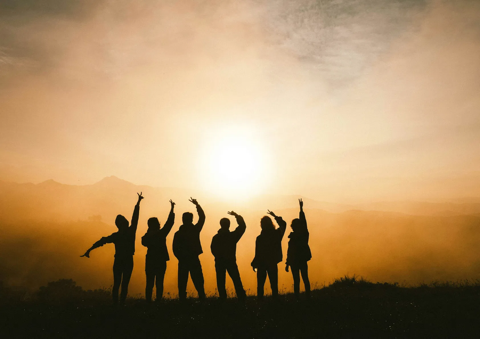 Groupe de personnes de dos, face au lever du soleil, à la montagne