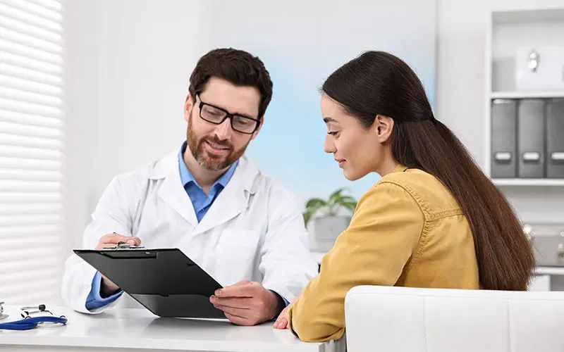 A physician listens to the heartbeat of a worker holding his yellow hard hat.