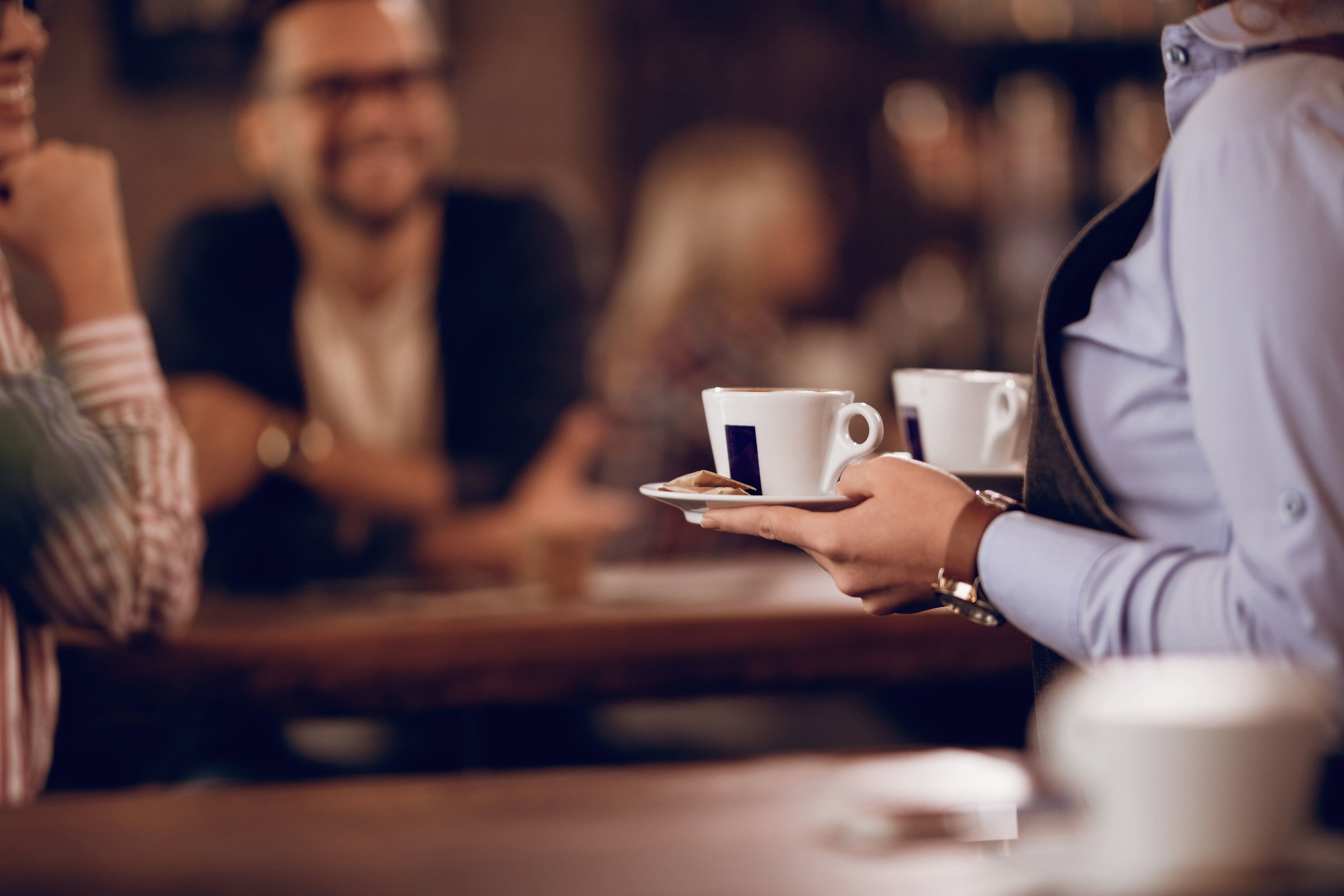 Photo d'une serveuse qui sert deux cafés à des clients au sein d'un café