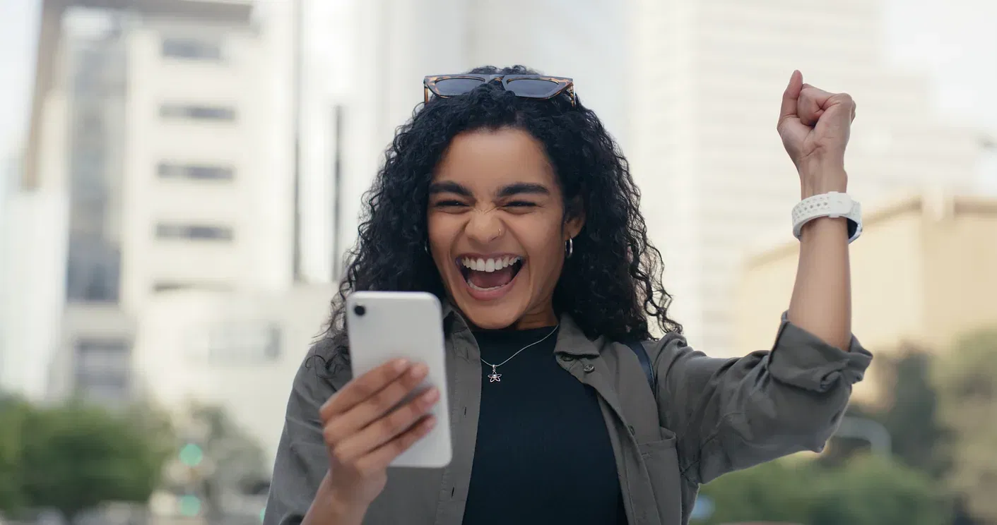 Excited woman smiling while holding phone after receiving good credit news