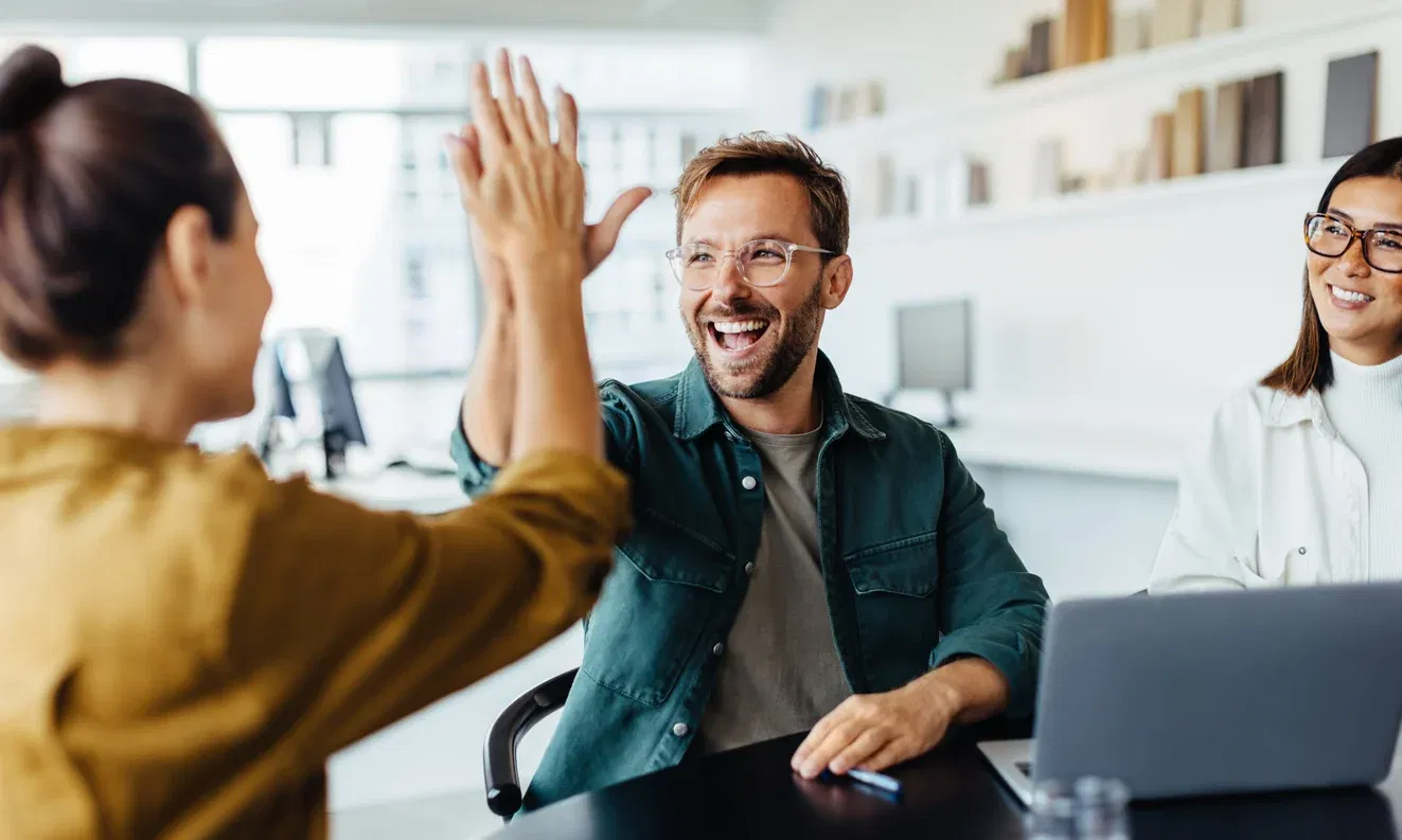 Man smiling and high-fiving woman while sitting with team around a laptop