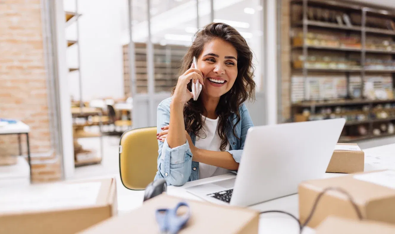 Smiling woman talking on phone in front of open laptop