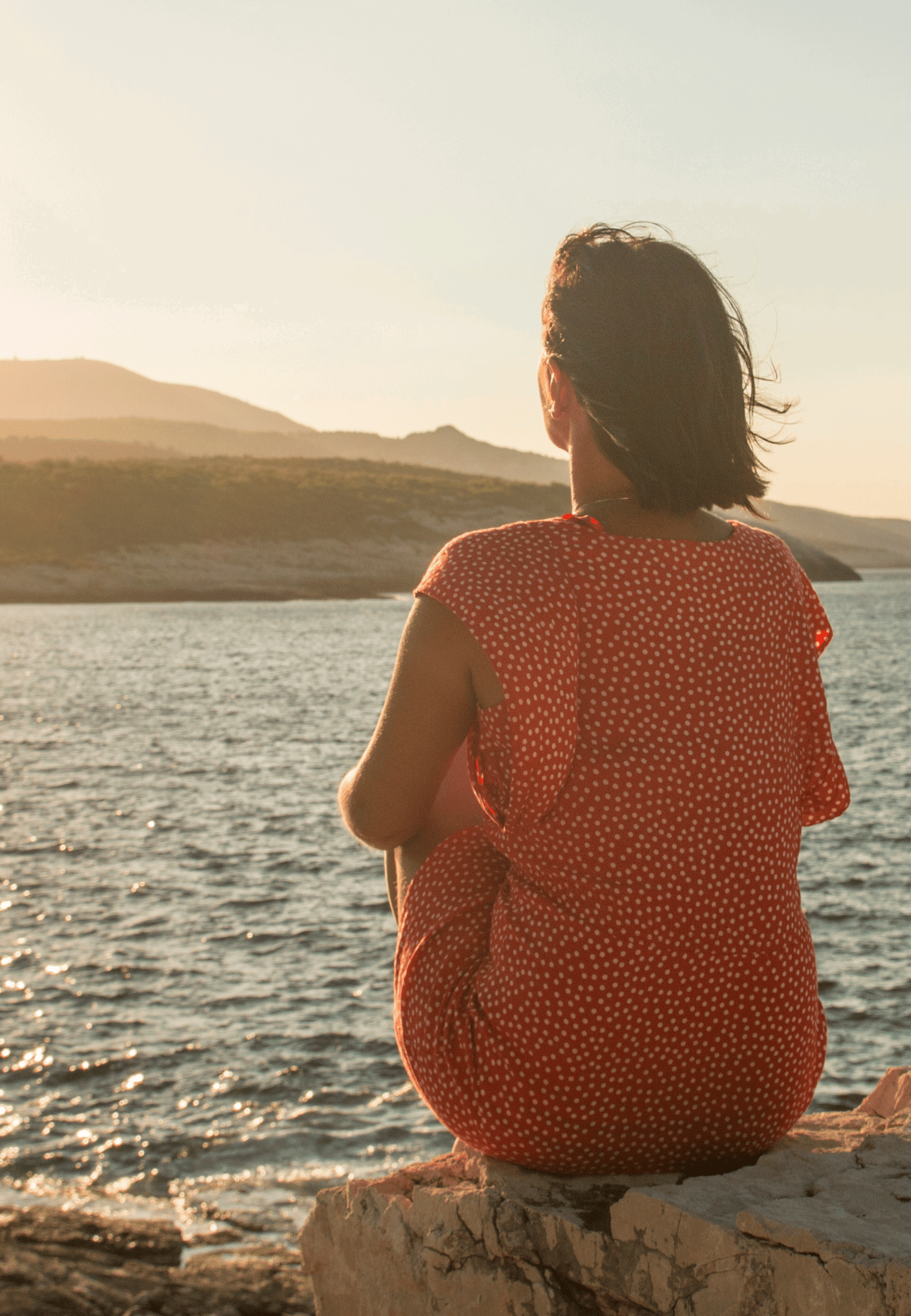Woman with brown hair wearing a red dress sitting down looking at the sunset