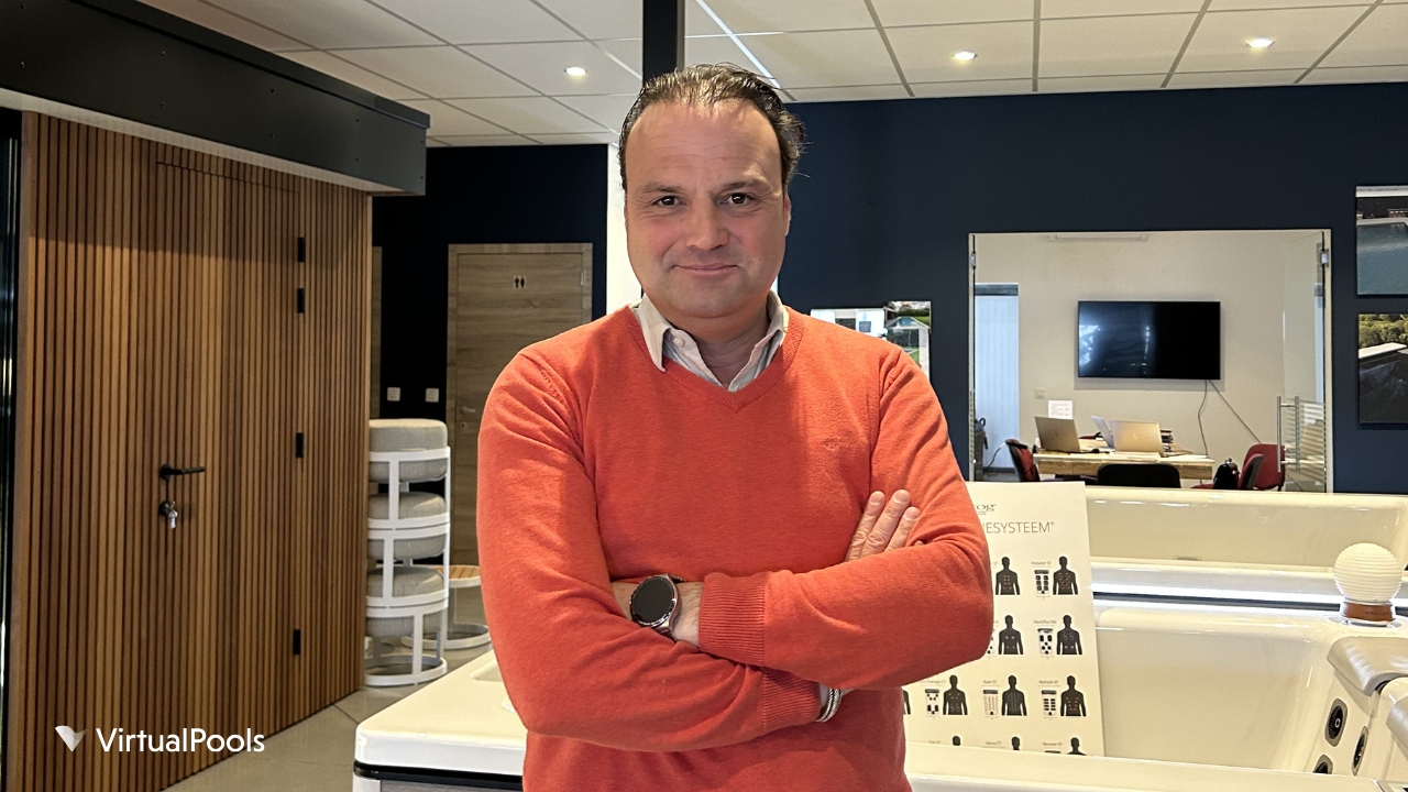 Michael Cop, the owner of Platinum Wellness stands with his arms crossed inside a modern showroom, with a hot tub, dark walls, wood paneling, and office space visible behind him.